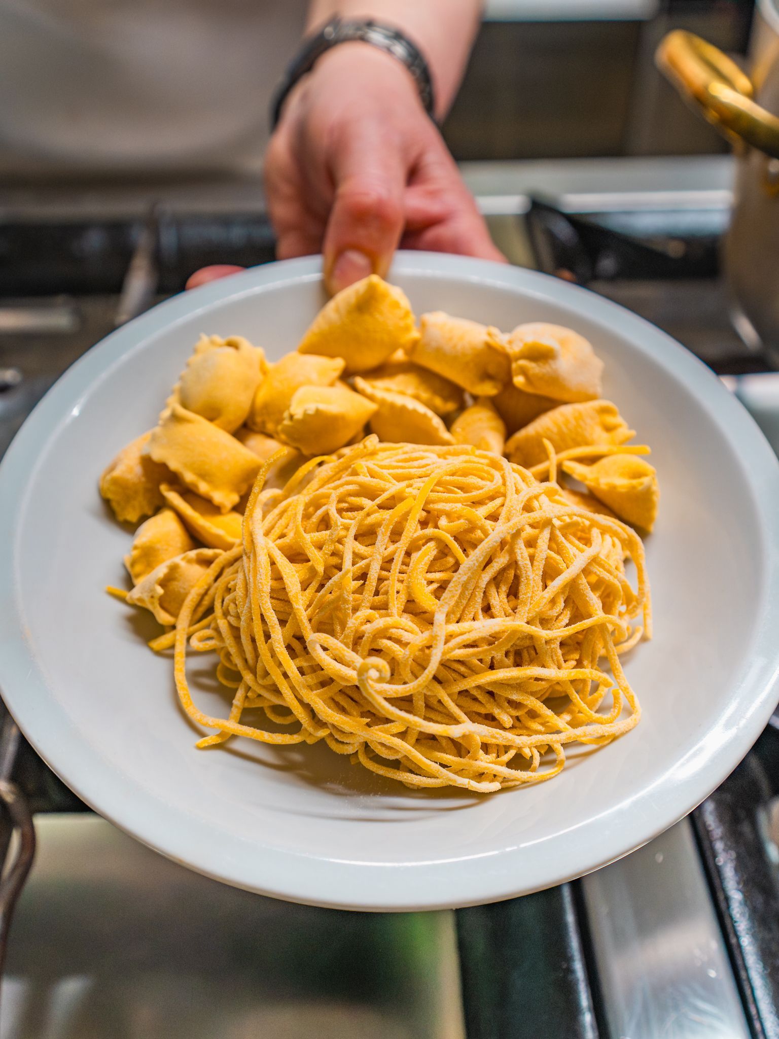 Piatto di spaghetti e ravioli su un fornello, sorretto da una mano.
