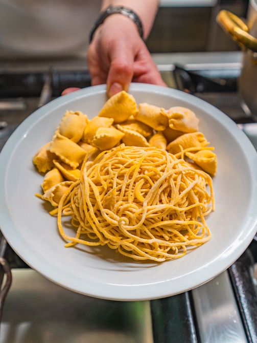 Piatto di spaghetti e ravioli su un fornello, sorretto da una mano.