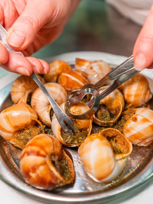 Mani che usano forchette per prendere le lumache da un vassoio di lumache cotte su un tavolo