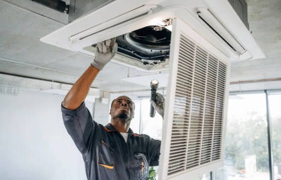 Technician repairing a ceiling air conditioner with the access panel open
