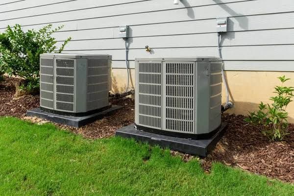 Two outdoor air conditioning units beside a house on a lawn