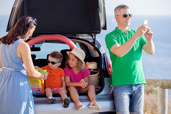 Family by open car trunk at the coast. Father taking photo, mother handing a drink, children sitting. | Morin Brothers Automotive