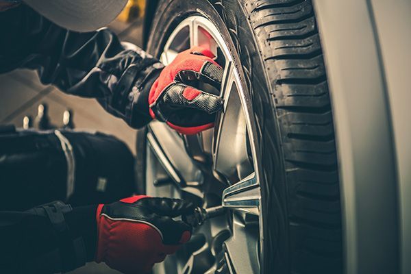 Mechanic tightening lug nuts on a car tire, wearing red gloves, in a garage. | Morin Brothers Automotive