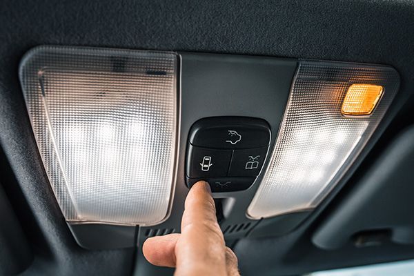 Hand presses the central locking button on a car's overhead console with lights. | Morin Brothers Automotive