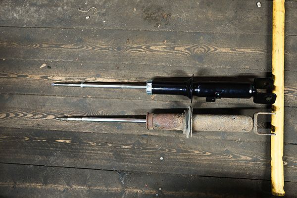 Two car shock absorbers, new and old, on a wooden surface. | Morin Brothers Automotive