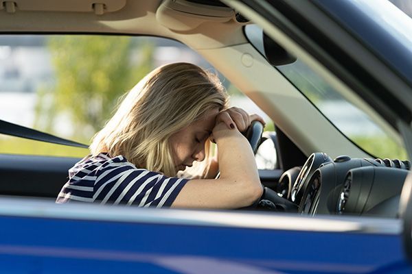 Woman resting her head on steering wheel inside blue car. | Morin Brothers Automotive