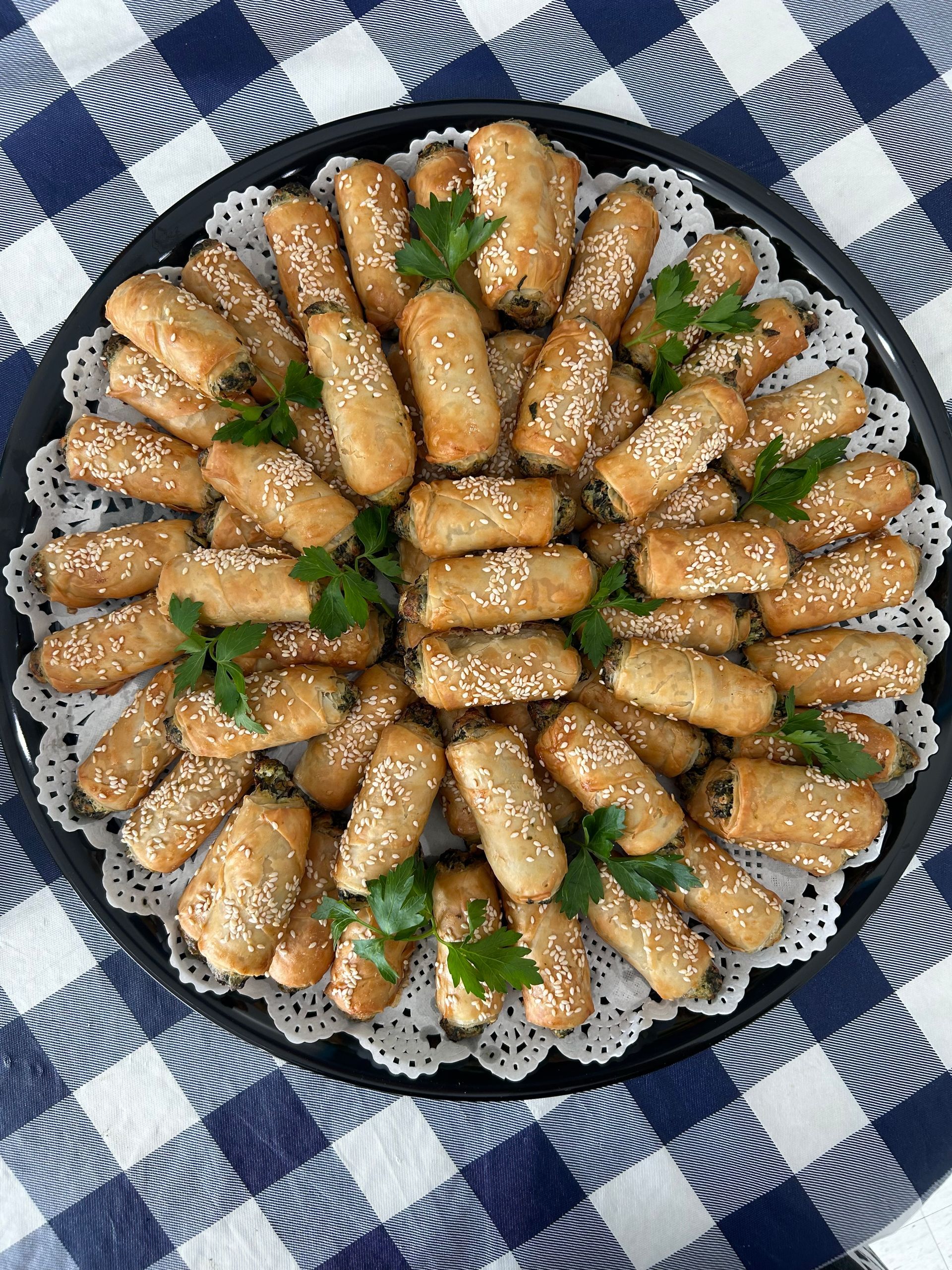 Plated sesame-coated finger pastries arranged in a flower shape on a blue-and-white checkered cloth.