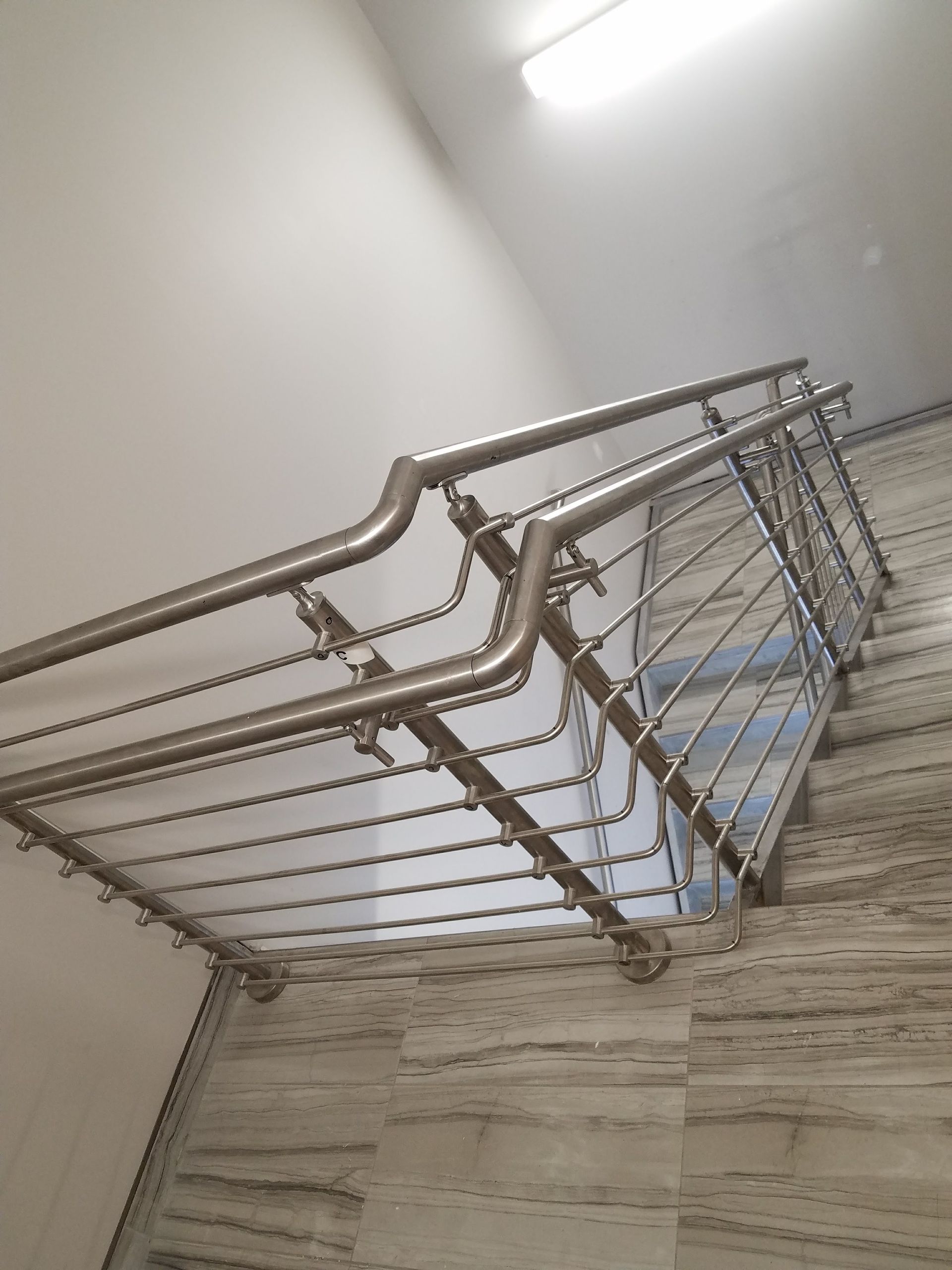 Metal stair railing beside a light wood staircase in a bright indoor hallway