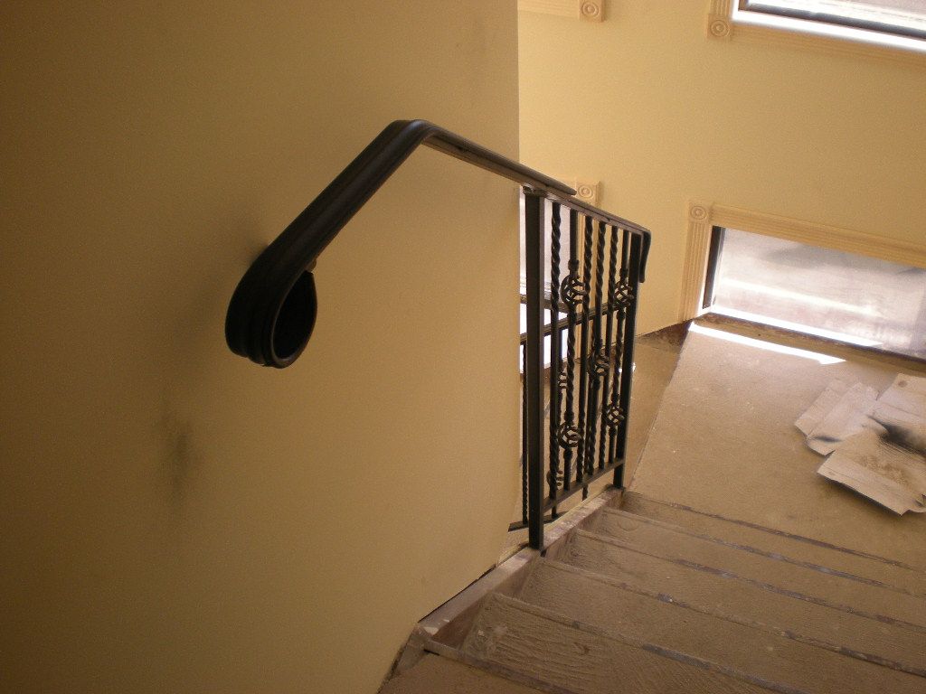 Staircase with black metal handrail and beige carpet, lit by sunlight from a nearby window.