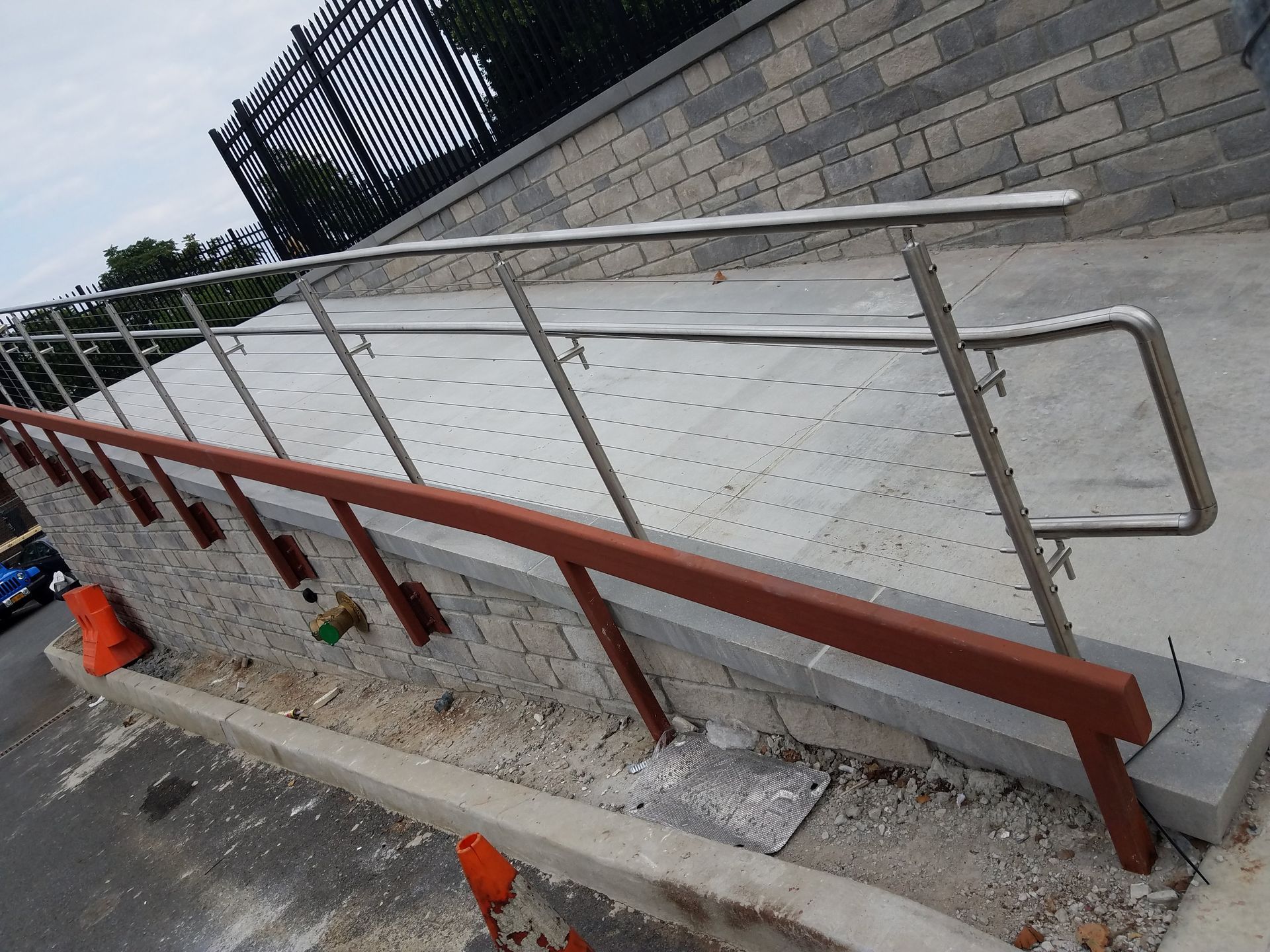 Concrete accessibility ramp with metal handrails beside a stone wall and curb