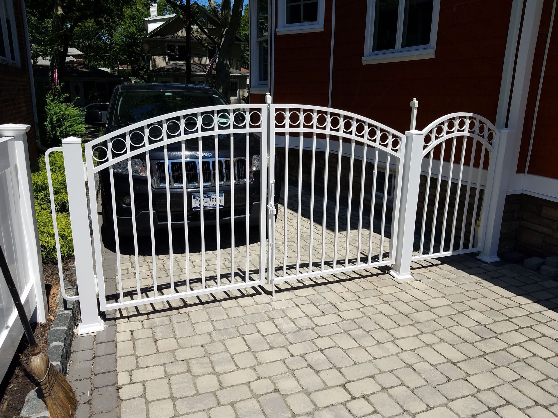 White curved metal driveway gate in front of a brick house and parked car.