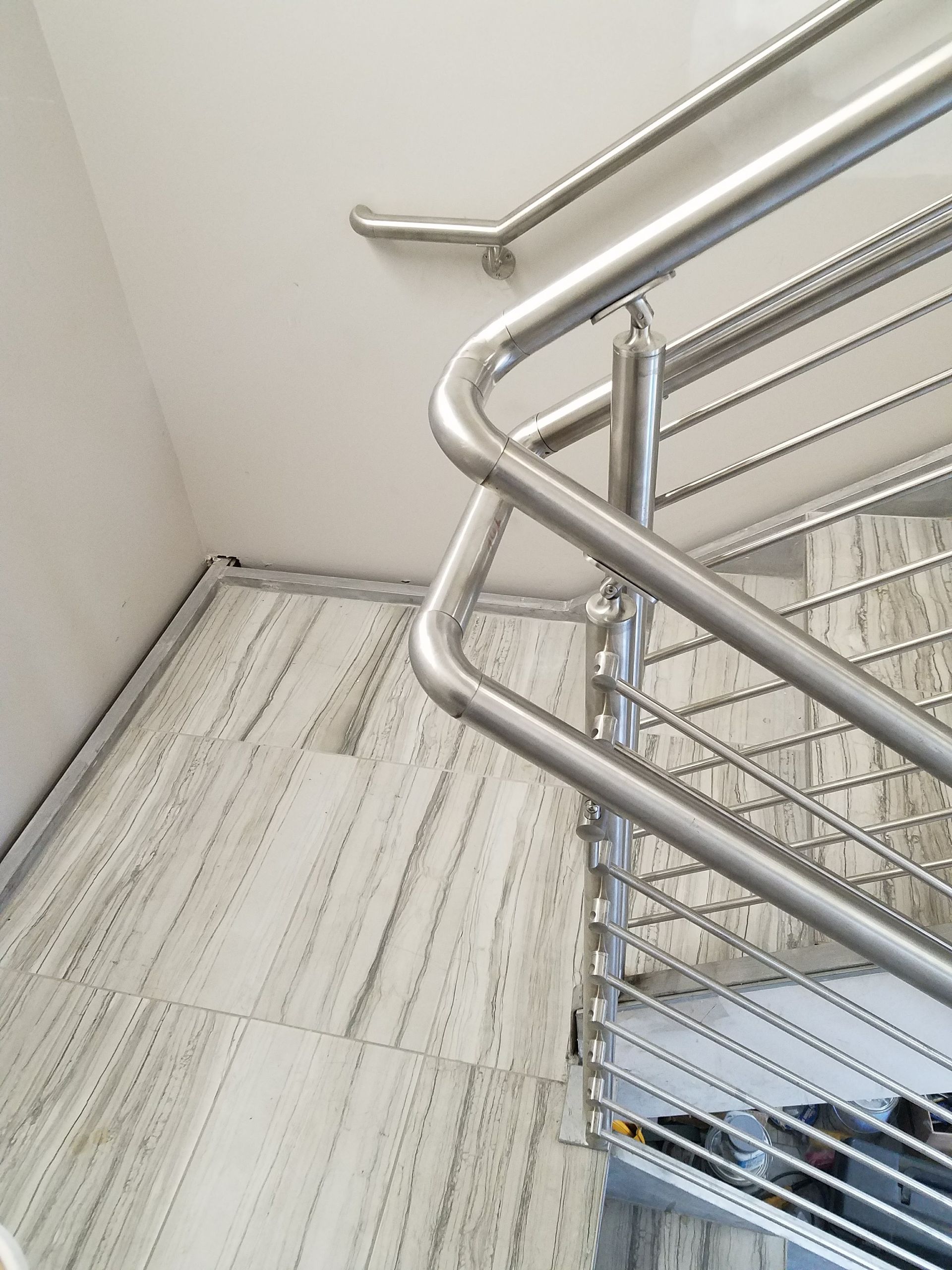 Stainless steel stair railing beside a light-colored wall and tiled floor in a stairwell.