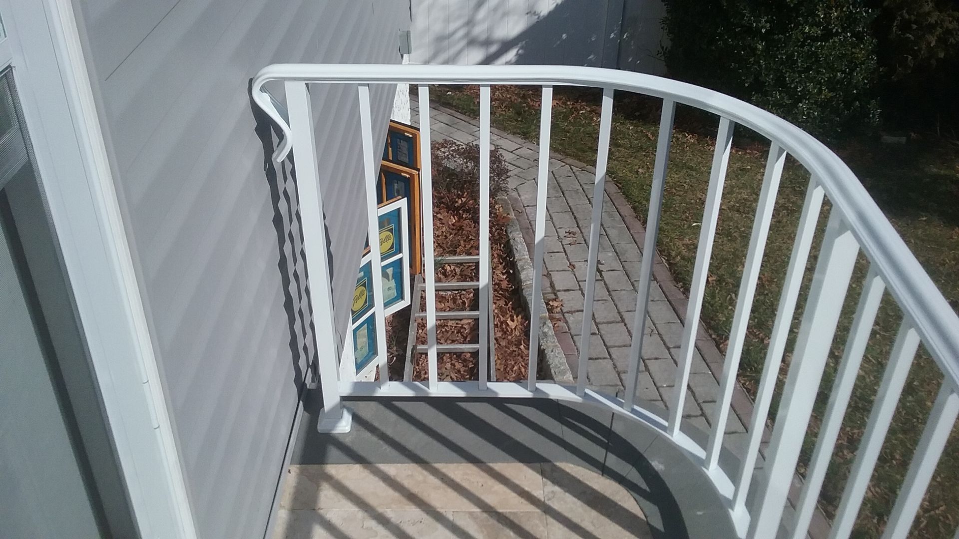 White spiral staircase with gray steps and white railing beside a house, viewed from above.