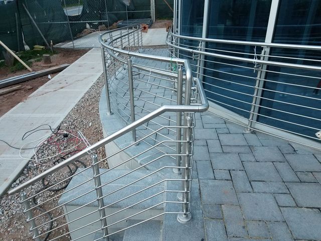 Accessible metal ramp with silver handrails beside a building walkway and blue wall.