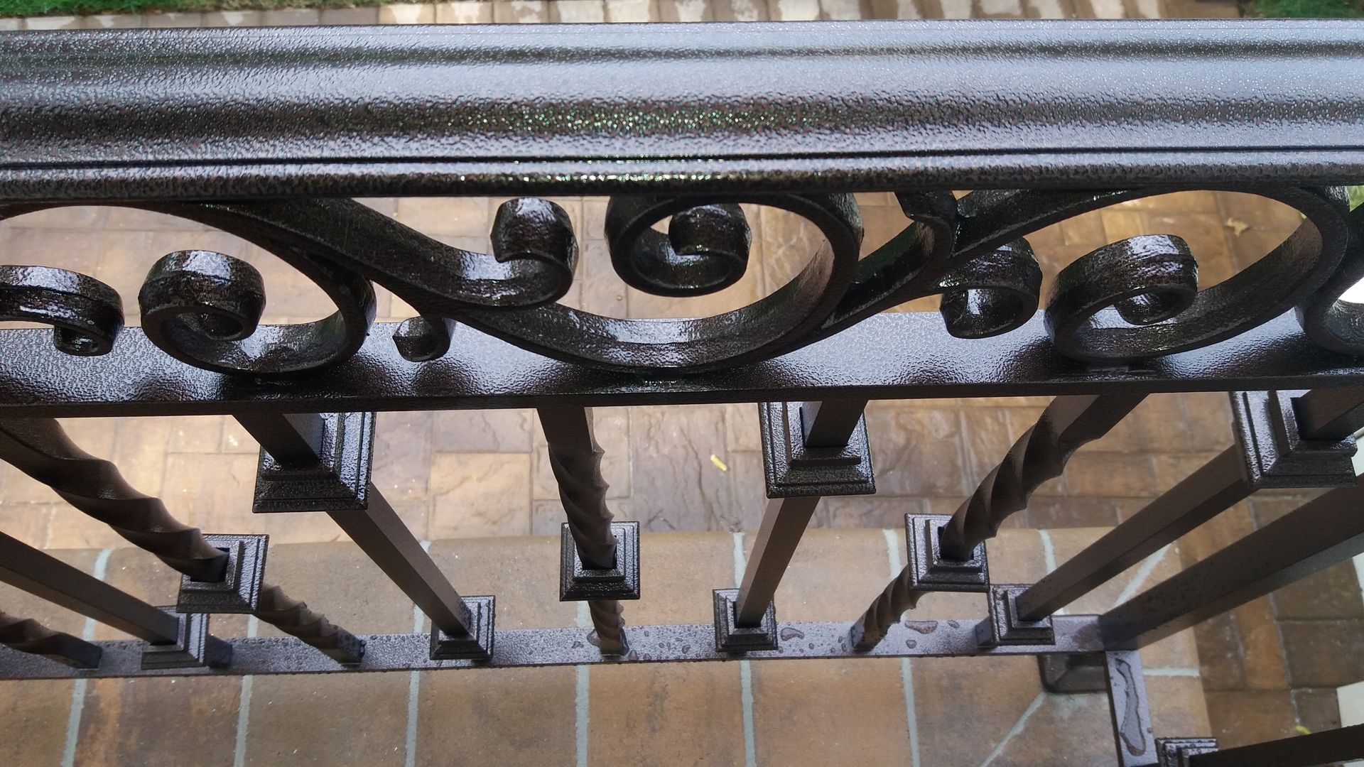 Black wrought-iron railing with decorative scrollwork above a tiled floor.