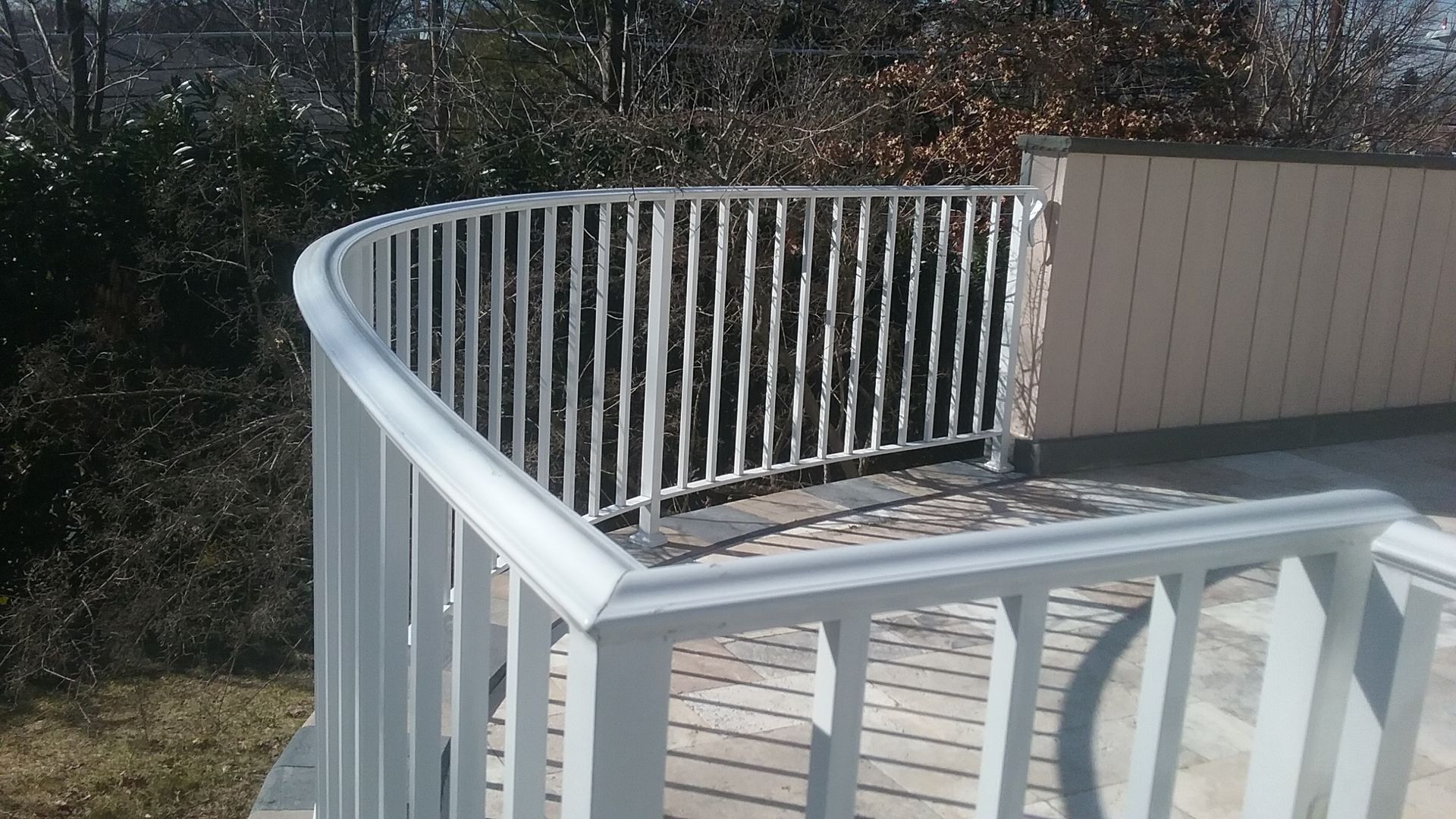 White curved railing on a deck overlooking trees and a beige privacy wall