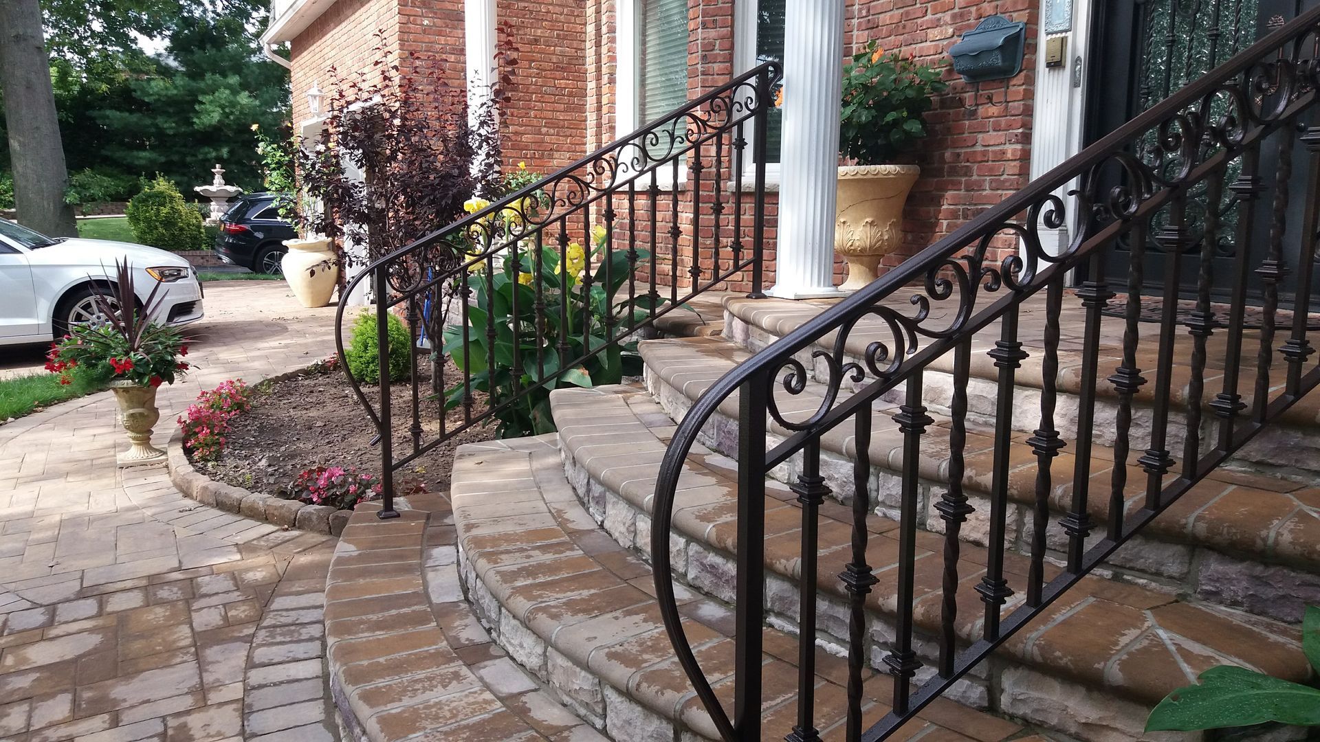 Brick townhouse entrance with curved stone steps, black iron railings, and landscaped front walkway.