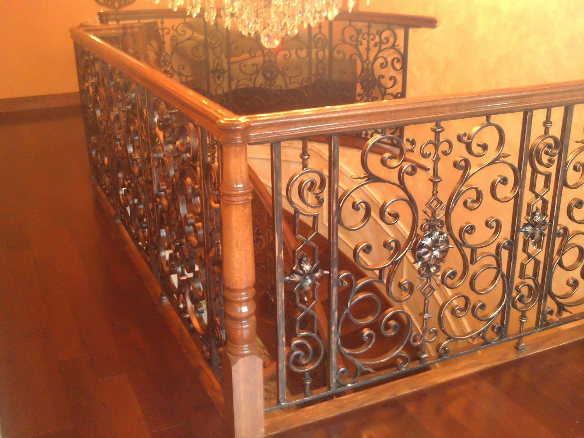Ornate wrought-iron stair railing beside a polished wooden banister in warm indoor lighting