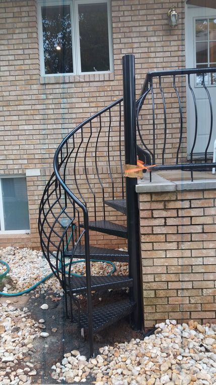 Curved black metal spiral staircase beside a brick house with scattered landscaping stones