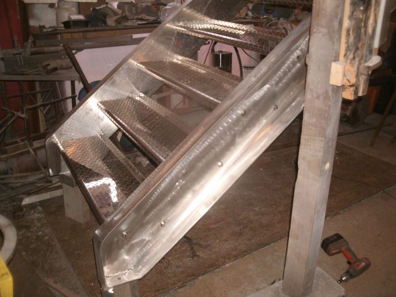 Shiny metal stair section under construction in a workshop, with unfinished steps and support frame
