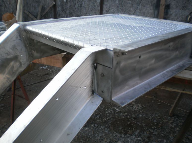 Metal rooftop hatch with diamond-plate lid and sloped aluminum sides on a structure outdoors