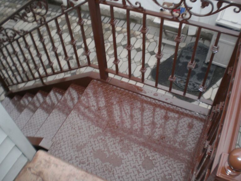 Stairwell landing with red patterned tile floor and brown metal railing casting shadows