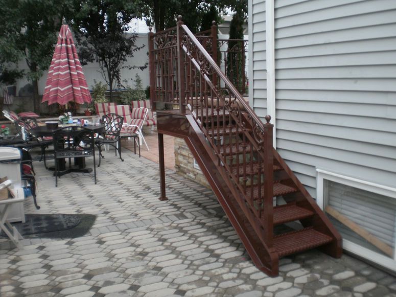 Patio with tables and umbrellas beside a building, featuring a red wooden staircase to an elevated entrance