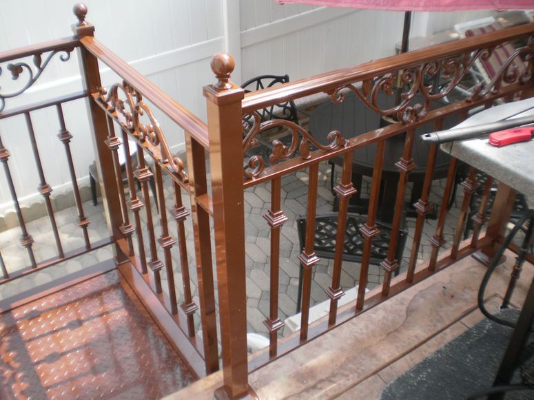 Wooden and metal staircase railing beside a tiled landing and a folded chair