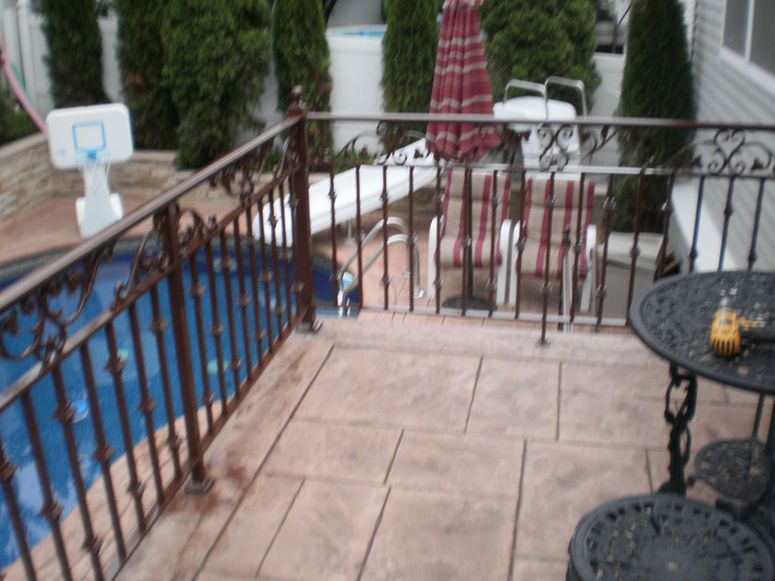 Patio with black metal railing, blue pool cover, and small round table beside potted shrubs