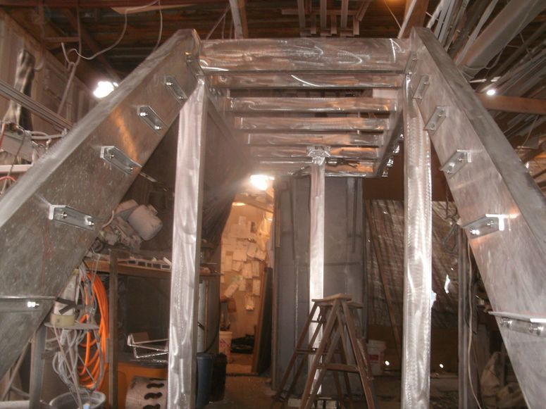 Metal framework under construction inside an industrial workshop with ladders and tools.