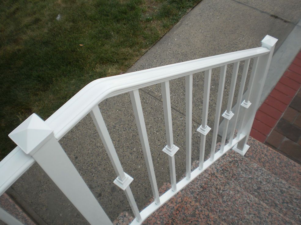 White porch railing with vertical balusters and a granite stair step beside a brick house.