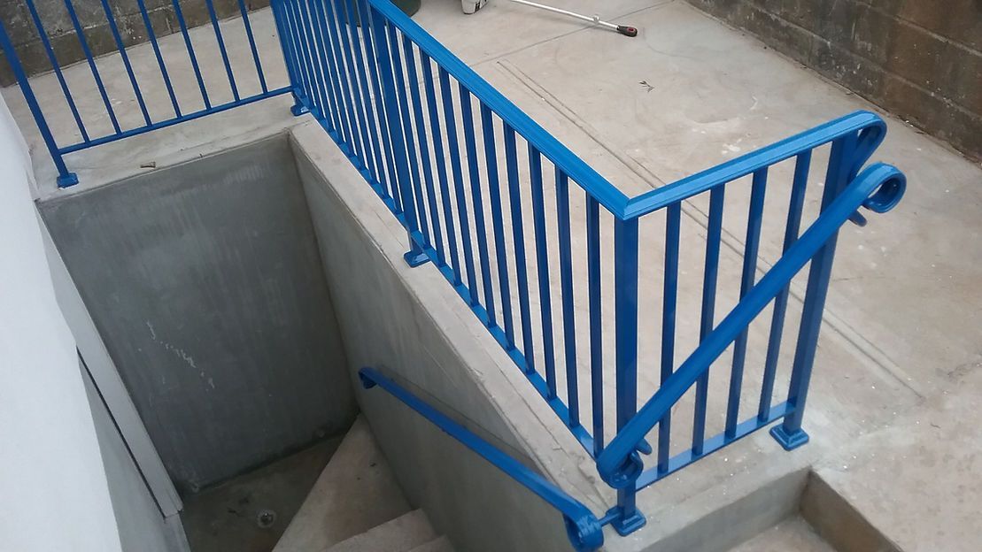Blue metal railing around a concrete stairwell opening indoors