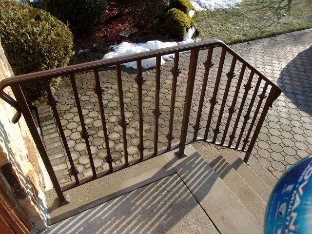 Curved metal railing beside sunlit stone steps leading to a paved walkway and garden area