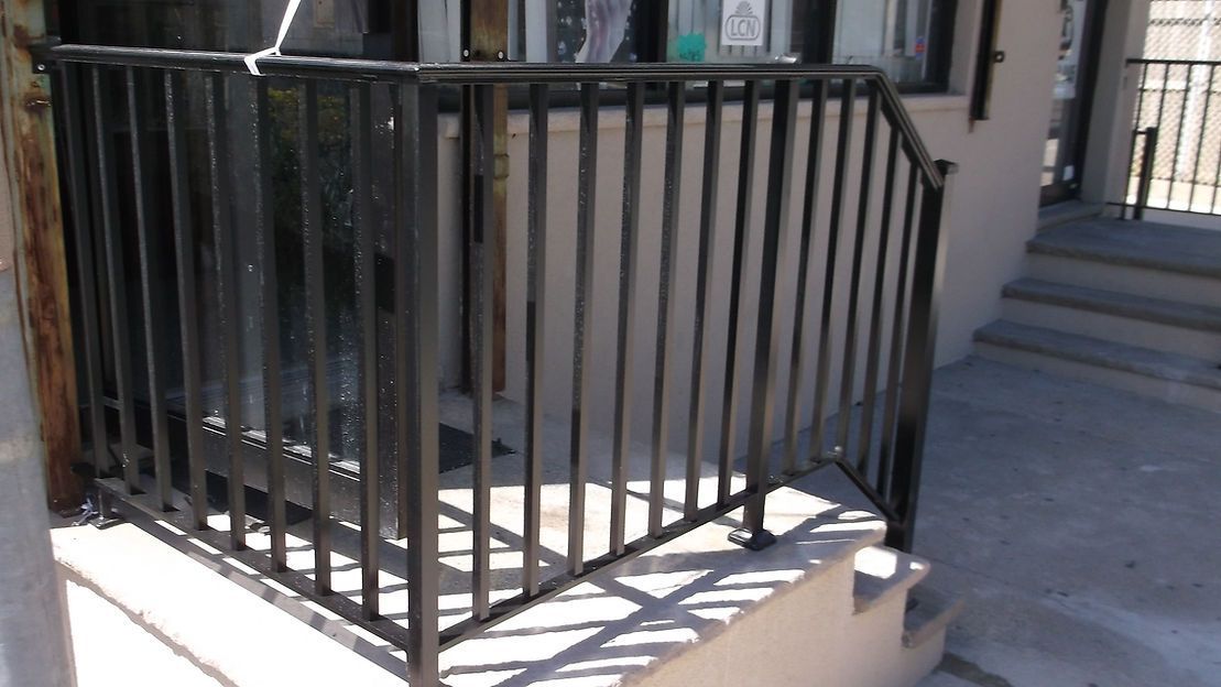 Black metal railing around a small concrete stair landing beside a building entrance