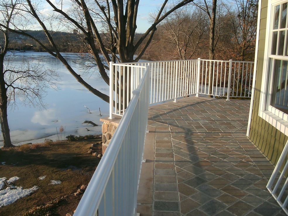 Stone patio with white railing overlooking a lake and bare trees in winter