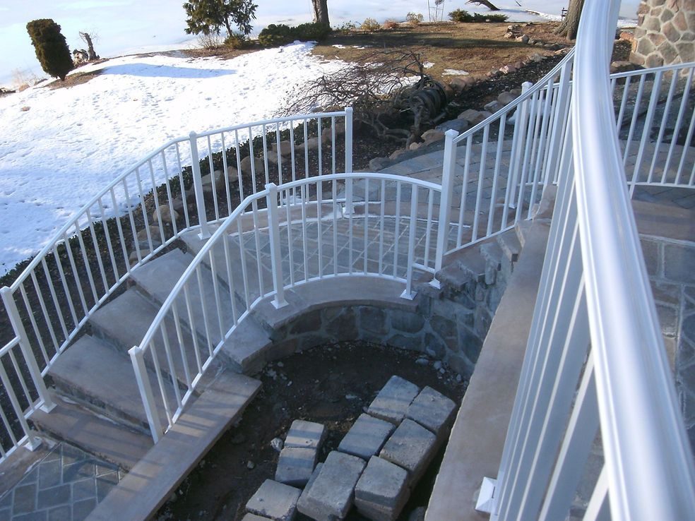 White curved ramp with railings descending over dark ground beside snow and stone steps