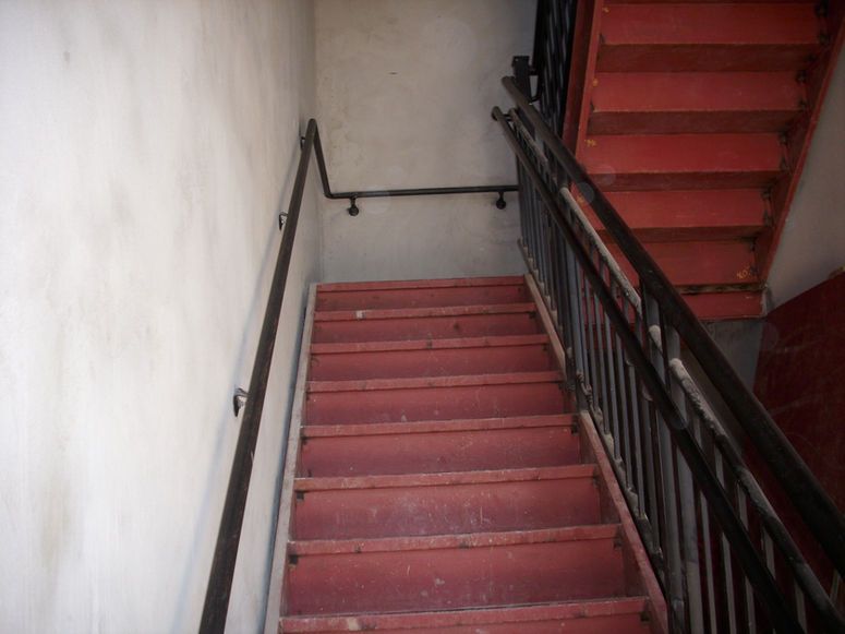 Red staircase with black railing in a narrow indoor stairwell.