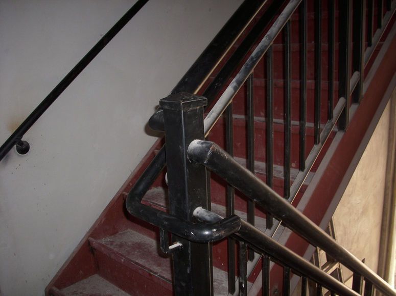 Stairwell with red steps and black metal handrail and balusters.