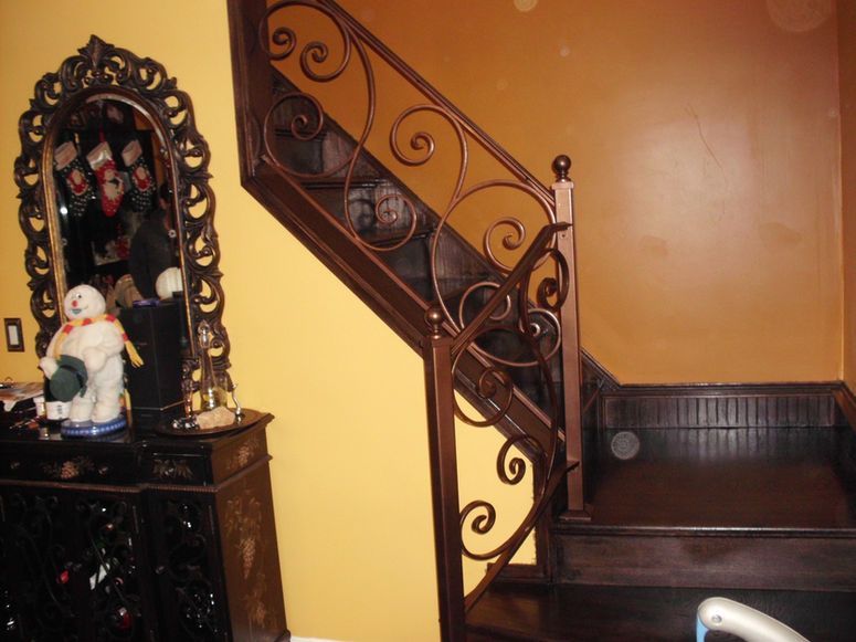 A staircase with ornate wrought-iron railing beside a decorative mirror and a small Santa figure on a dark cabinet