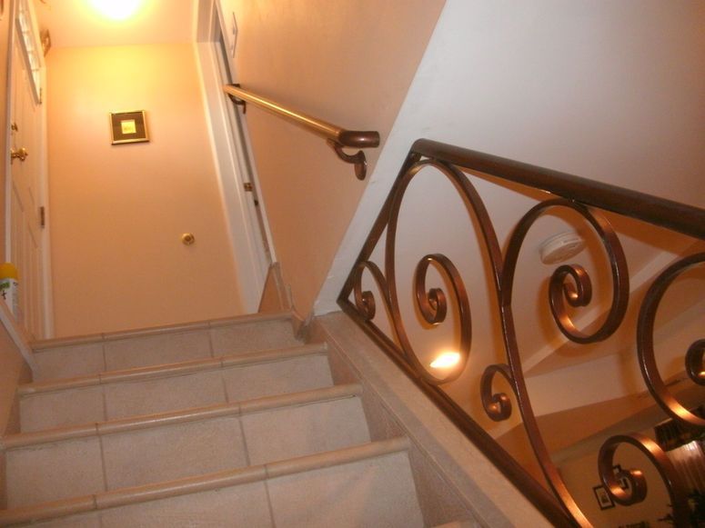Stairwell with beige steps, white walls, and ornate dark metal railing lit by warm wall lights