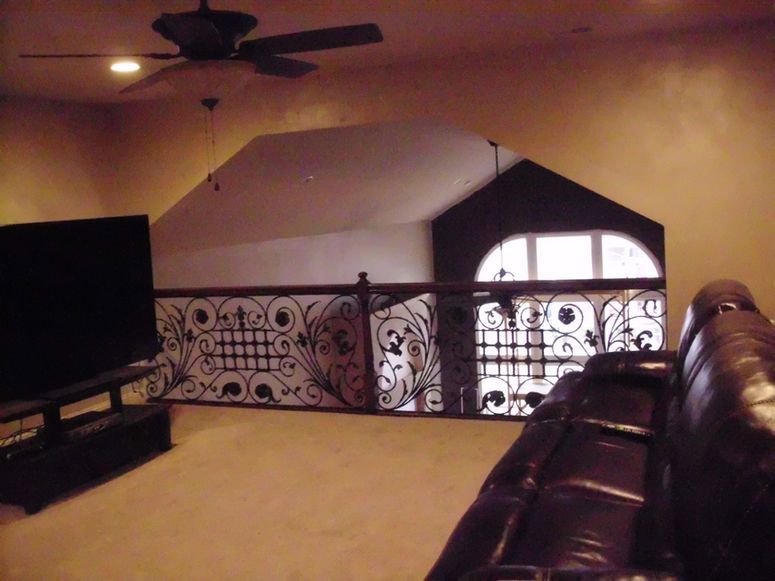 Loft living room with black TV, ceiling fan, and ornate iron railing overlooking a stairwell.