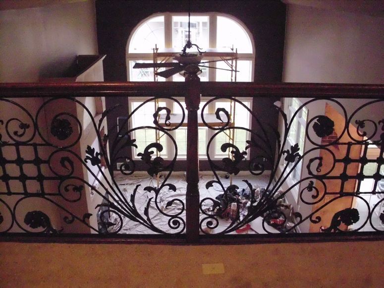 Ornate black wrought-iron balcony railing before a bright arched window in an indoor hallway