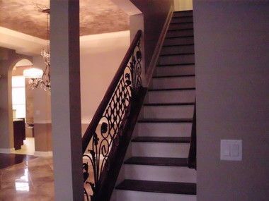 Indoor staircase with dark railing and patterned banister in a warmly lit hallway