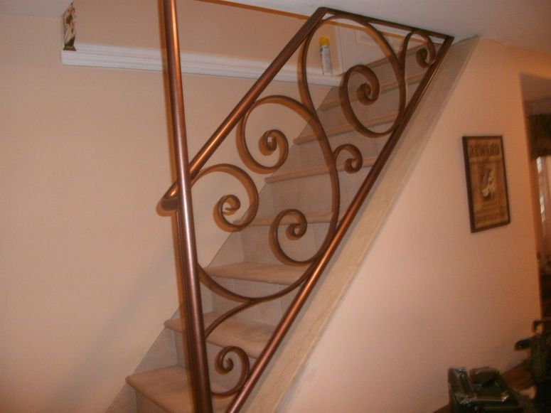 Decorative wrought-iron stair railing with scrollwork along a beige staircase wall