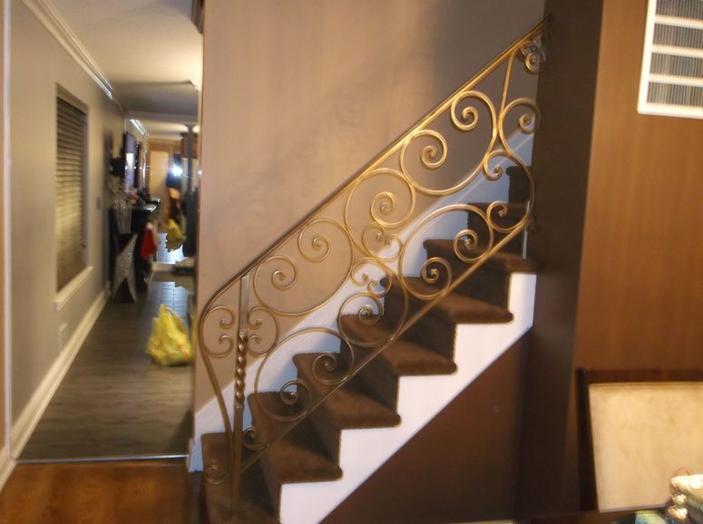 Indoor staircase with ornate railing in a narrow hallway beside a doorway and closet doors