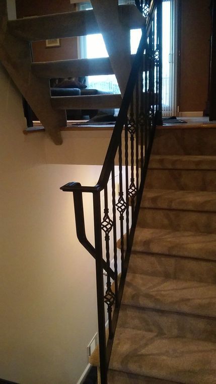 Indoor staircase with black wrought-iron railing beside carpeted steps and a windowed landing