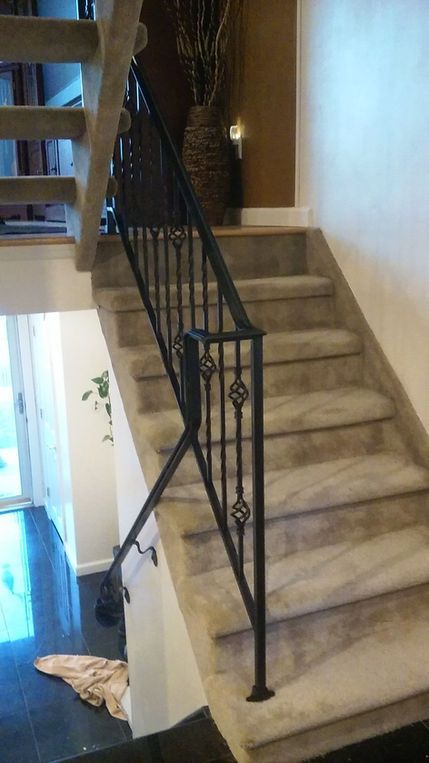 Indoor staircase with beige carpeted steps and a black wrought-iron railing.