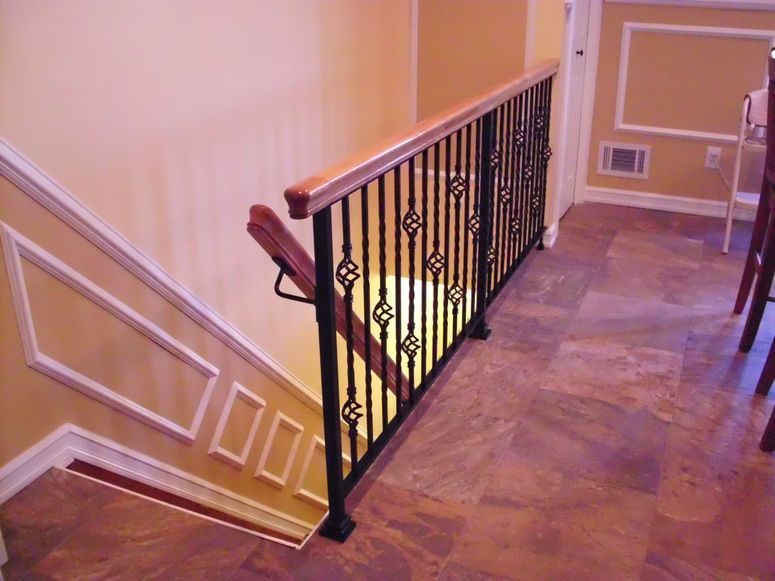 Indoor staircase with black wrought-iron railing and warm beige walls, lit from below.