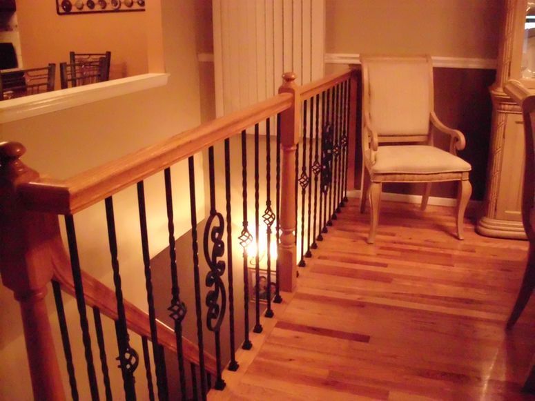 Warm-lit wooden staircase with black iron railing and chairs on a landing