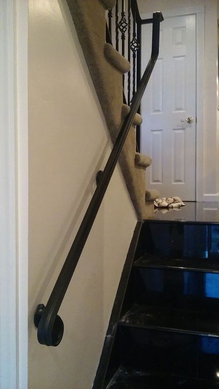 Stairway with black handrail and tan carpeted steps leading to a white door in a hallway